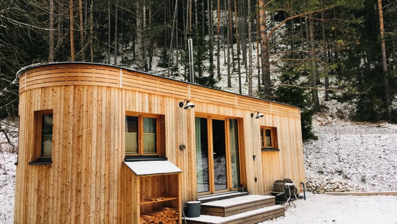 Ein Wohnwagon aus Holz steht im verschneiten Wald.