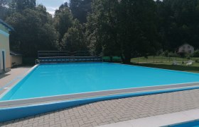Ein leerer Swimmingpool im Freien, umgeben von Bäumen und einem Gebäude.