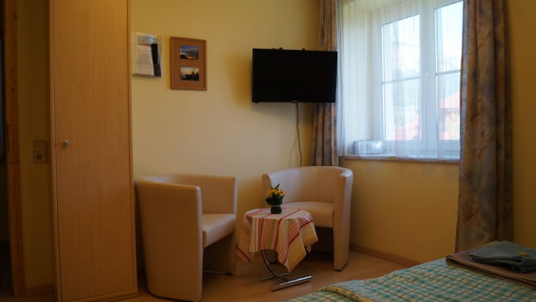 Gemütliche Sitzecke mit zwei Sesseln, kleinem Tisch und Fernseher in einem hellen Raum mit Fenster.