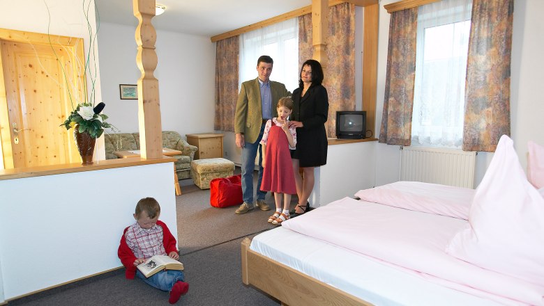 Familie in einem gemütlichen Hotelzimmer mit Holzmöbeln und rosa Bettwäsche.