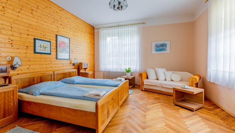 Gemütliches Schlafzimmer mit Holzwänden, zwei Betten, Sofa und Holzboden.