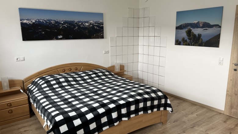 Schlafzimmer mit Doppelbett, kariertem Bettüberwurf, Holzmöbeln und Berglandschaftsbildern an der Wand.