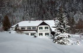 Ein verschneites Gebäude namens Gschaiderhof vor einem Wald im Winter.