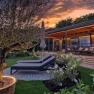 Ein modernes Chalet mit Terrasse und Liegestühlen im Garten bei Sonnenuntergang.