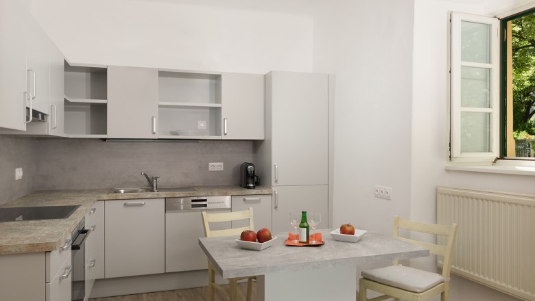 Moderne Küche mit grauen Schränken, Tisch mit Äpfeln und Getränk, offenes Fenster.