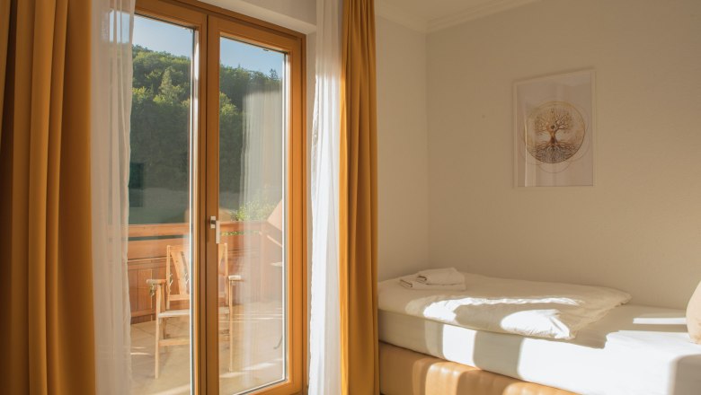 Einzelzimmer mit Balkon, Bett, gelbe Vorhänge, Holzbalkon, sonnig.