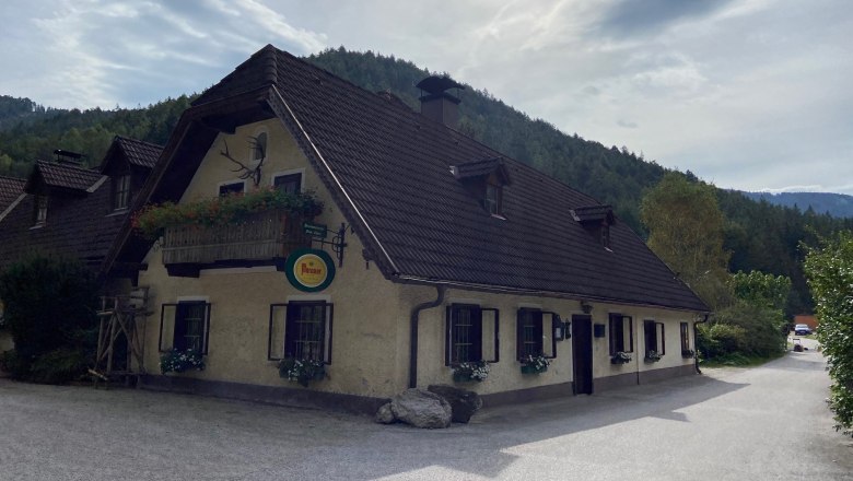 Traditionelles Gasthaus mit Blumenbalkon vor bewaldeten H&uuml;geln.