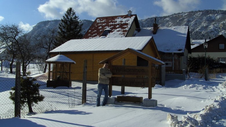 Winterlandschaft mit schneebedecktem Haus und Bergen im Hintergrund.