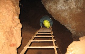 Person mit Helm klettert eine Leiter in einer H&ouml;hle hinunter.