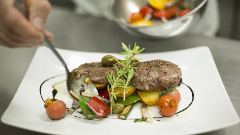 Ein Teller mit kunstvoll angerichtetem Fleisch, Gemüse und Kräutern.