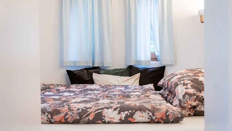 Gemütliches Schlafzimmer mit floralem Bettzeug und blauen Vorhängen.