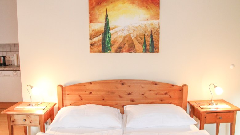 Schlafzimmer mit Holzbett, zwei Nachttischen und einem Landschaftsbild an der Wand.
