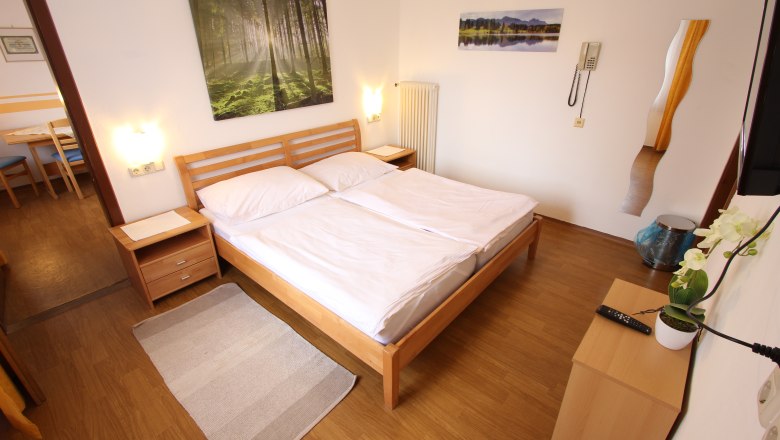 Helles Schlafzimmer mit Doppelbett, Holzmöbeln und Naturbildern an der Wand.