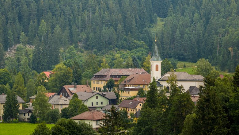Ein Dorf mit Kirche inmitten von bewaldeten Bergen.