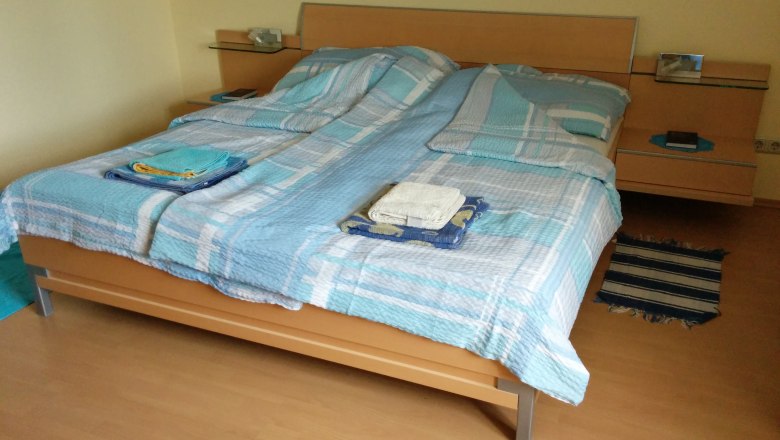 Doppelbett mit blauer Bettwäsche in einem Zimmer mit Holzboden.