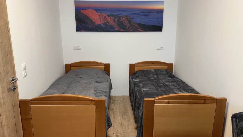 Ein einfach eingerichtetes Zimmer mit zwei Einzelbetten und einem Landschaftsbild an der Wand.