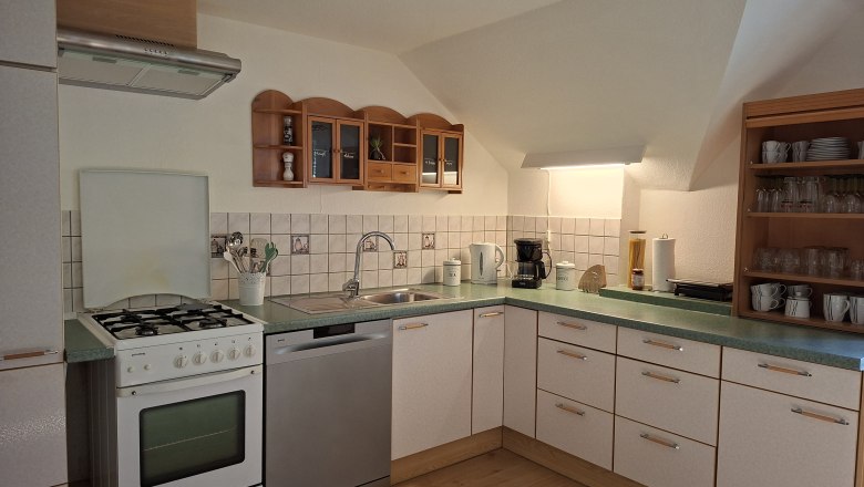 Eckk&uuml;che mit Herd, Sp&uuml;le, Geschirrsp&uuml;ler und Regalen.