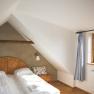 Gemütliches Schlafzimmer mit Dachschräge, Doppelbett, Holzdetails und Fenster mit Vorhang.