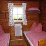 Holzvertäfeltes Zimmer mit zwei Einzelbetten, rot-weiß karierten Bettdecken und einem Fenster mit Blumenvorhängen.