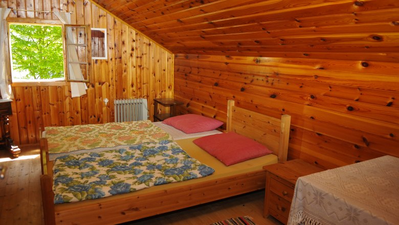 Holzvertäfeltes Schlafzimmer mit Doppelbett, bunten Decken und offenem Fenster.