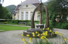 Brunnen vor einem historischen Gebäude mit gelben Blumen im Vordergrund.