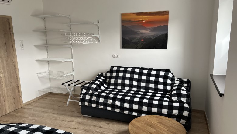 Schlafzimmer mit kariertem Sofa, Wandregal und Landschaftsbild.