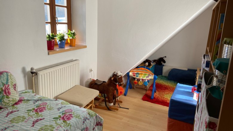 Kinderzimmer mit Bett, Spielzeug und buntem Teppich.