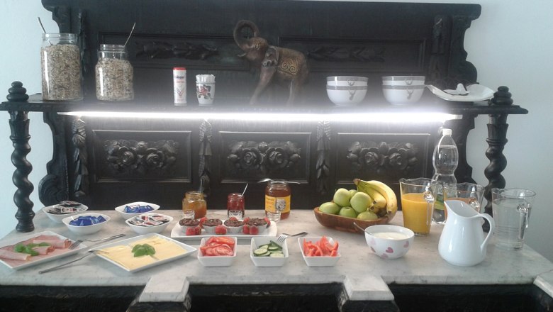 Frühstücksbuffet mit Obst, Aufschnitt, Käse, Marmelade und Getränken auf einem dekorativen Tisch.