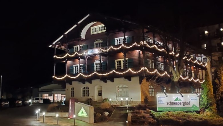 Ein beleuchtetes Gebäude namens Schneeberghof bei Nacht, dekoriert mit Lichterketten.