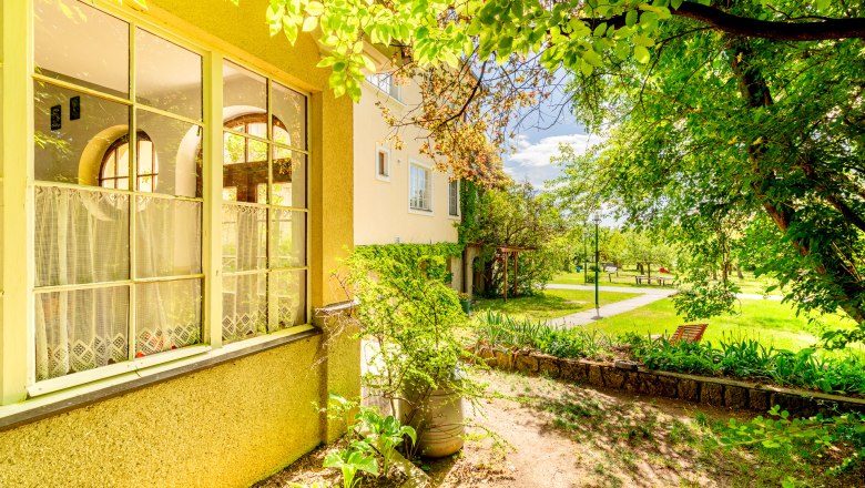 Ein Herrenhaus mit großen Fenstern und einem gepflegten Garten im Sonnenschein.