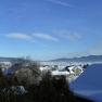 Winterlandschaft mit schneebedeckten Dächern und Bergen im Hintergrund.