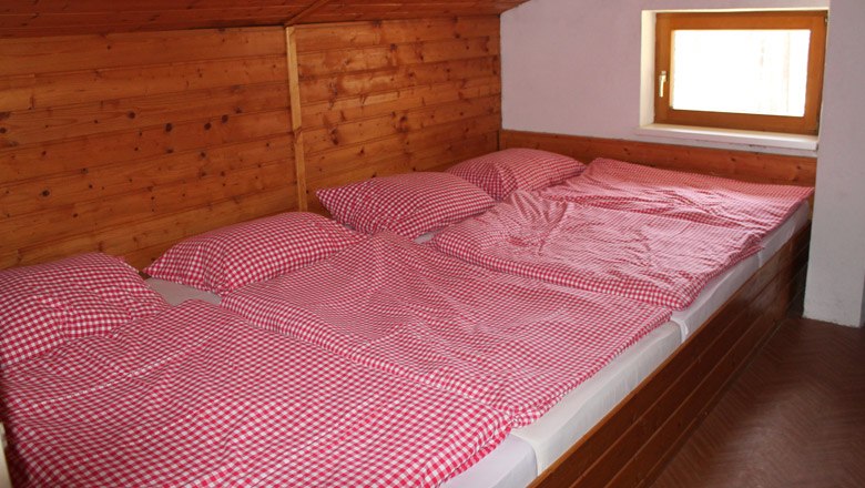 Drei Betten mit rot-weiß karierten Bettbezügen in einem holzverkleideten Raum.