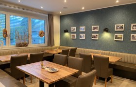 Innenansicht eines Restaurants mit Holztischen, gepolsterten Stühlen und einer Wand mit gerahmten Bildern.