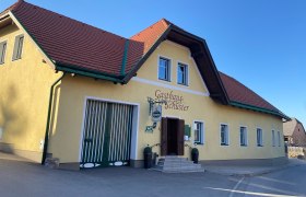 Gelbes Gebäude mit rotem Dach, beschriftet als Gasthaus Schuster.