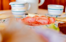 Nahaufnahme eines Frühstückstisches mit Schinken, Geschirr und Tassen.