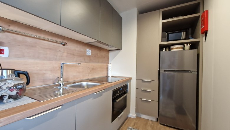 Moderne Küche mit grauen Schränken, Edelstahlspüle, Herd und Kühlschrank.