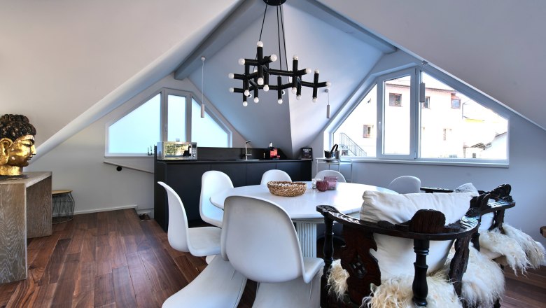 Moderner Essbereich in einem Dachgeschoss mit wei&szlig;en St&uuml;hlen, Holzboden und einem gro&szlig;en Fenster.