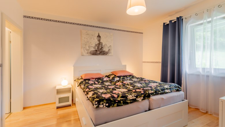 Gem&uuml;tliches Schlafzimmer mit Doppelbett, Nachttischlampe und Buddha-Bild an der Wand.