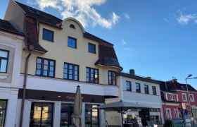 Au&szlig;enansicht eines Caf&eacute;s mit Terrasse und Sonnenschirm vor einem mehrst&ouml;ckigen Geb&auml;ude.