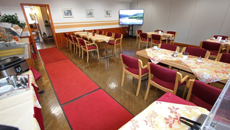 Ein Konferenzraum mit gedeckten Tischen, roten Stühlen und einem großen Bildschirm.