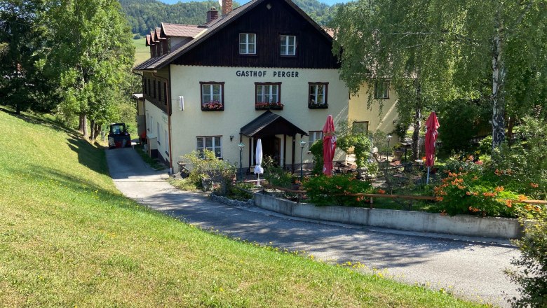 Ein traditionelles Gasthaus mit Terrasse und Sonnenschirmen, umgeben von grüner Landschaft.