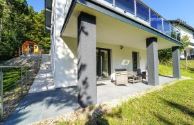 Terrasse eines modernen Ferienhauses mit Gartenmöbeln und angrenzendem Garten.