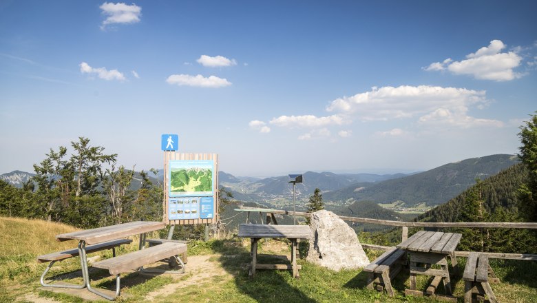 Aussichtspunkt mit Holzbänken und Infotafel in den Bergen.