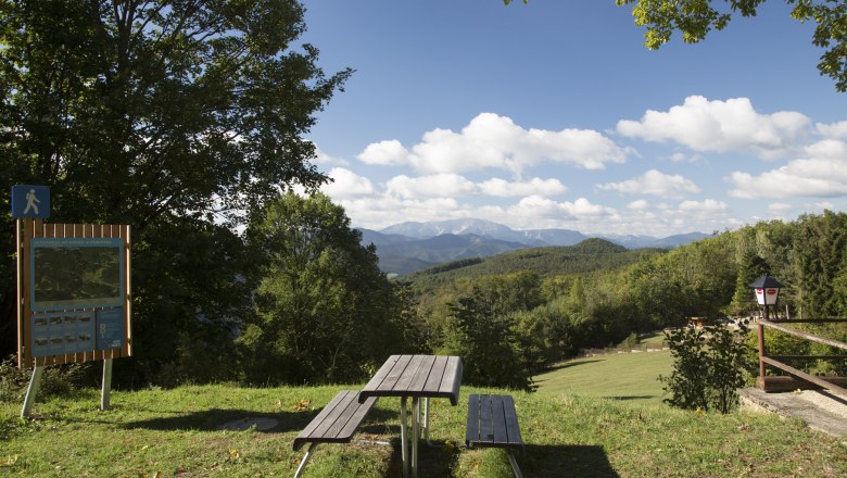 Picknicktisch mit Blick auf bewaldete Hügel und Berge, blauer Himmel mit Wolken.