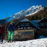 Zwei Skifahrer vor der Edelweissh&uuml;tte am Schneeberg mit schneebedecktem Berg im Hintergrund.