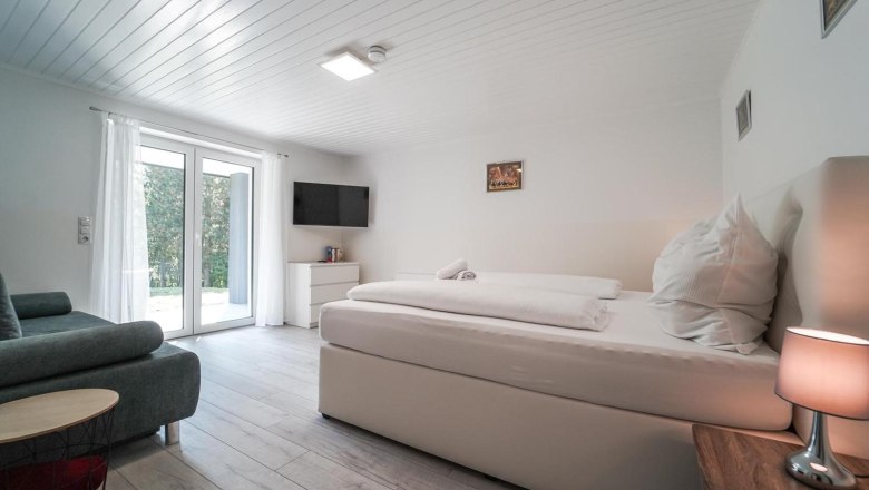 Modernes Schlafzimmer mit großem Bett, Sofa, Fernseher und Glastür.