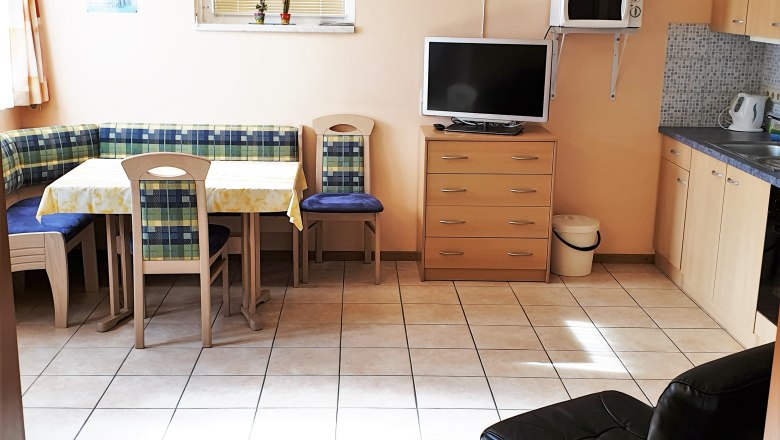 Küche mit Eckbank, Tisch, Stühlen, Fernseher, Mikrowelle und Schränken.