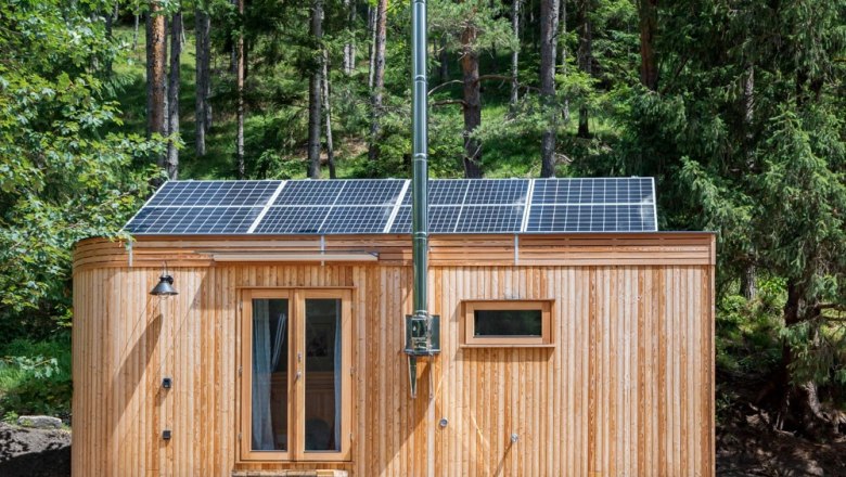 Kleines Holzhaus mit Solarpanelen auf dem Dach im Wald.