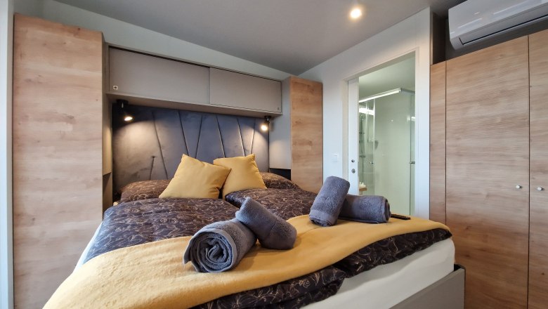 Modernes Schlafzimmer mit Doppelbett, gelben Kissen und Handtüchern, Holzschränken und Klimaanlage.