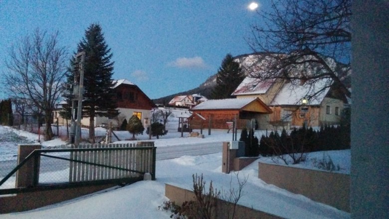 Winterliche Landschaft mit schneebedeckten Häusern und Bäumen bei Dämmerung.